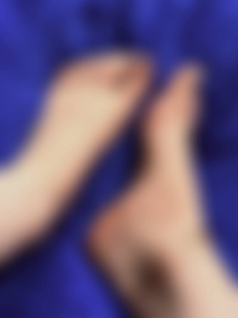 Bare feet with softly painted white toes rest against a smooth blue background, creating a